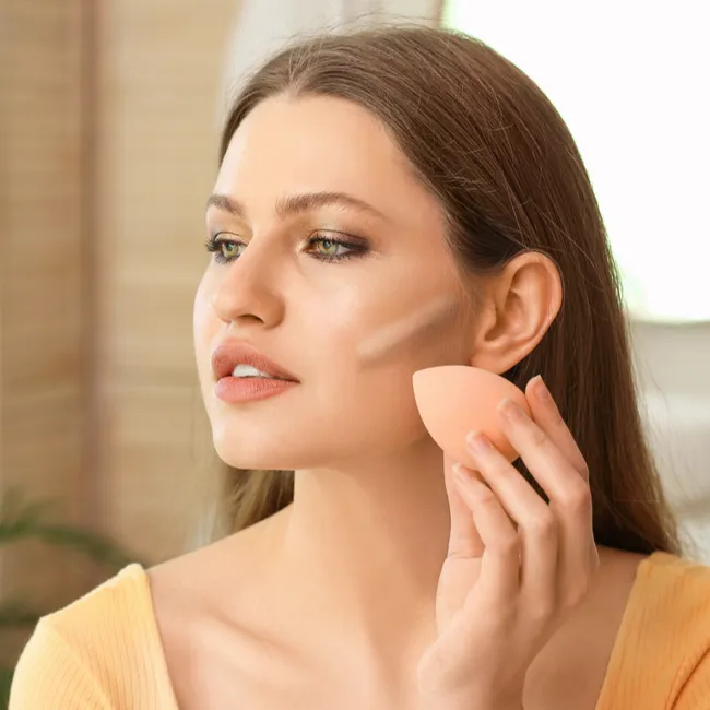 woman applying concealer to contour face with beauty blender