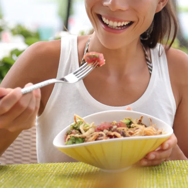 woman eating fish protein bowl hawaii brown hair ponytail white tank top yellow bowl fork