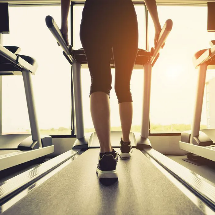 legs of woman walking on treadmill at gym