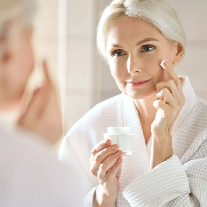 older mature woman applying sunscreen bathroom mirror robe