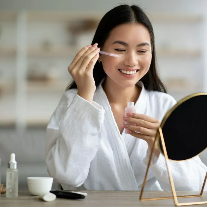 woman holding serum to under-eye area looking in cosmetic mirror
