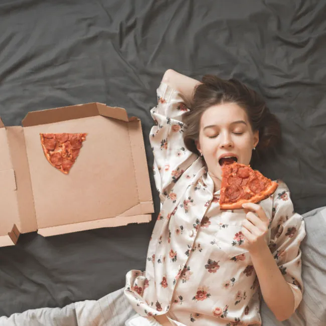 woman eating pepperoni pizza in bed