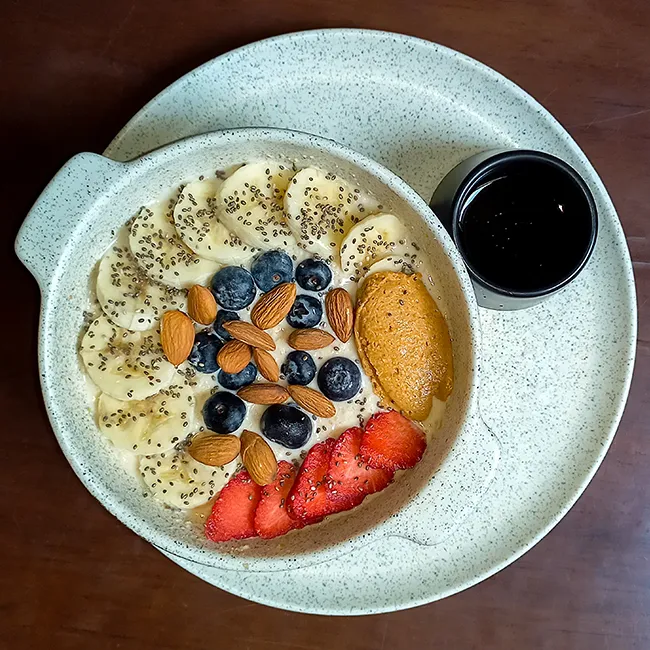 "Bowl of oatmeal topped with almonds, banana, blueberries, strawberries, chia, and peanut butter"
