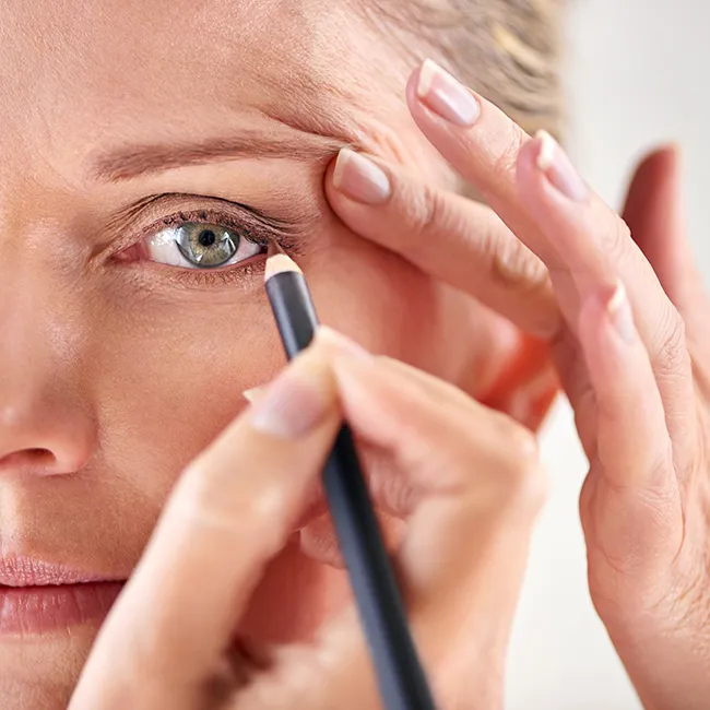 Middle-aged woman applying eyeliner for a polished look.