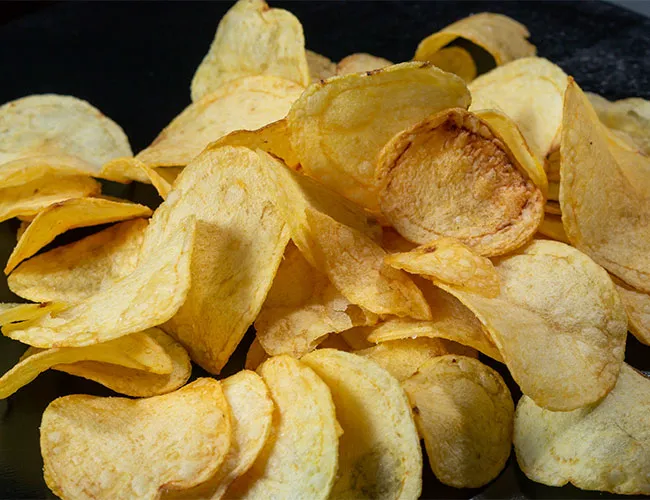 "A hand reaching for a bowl of potato chips"